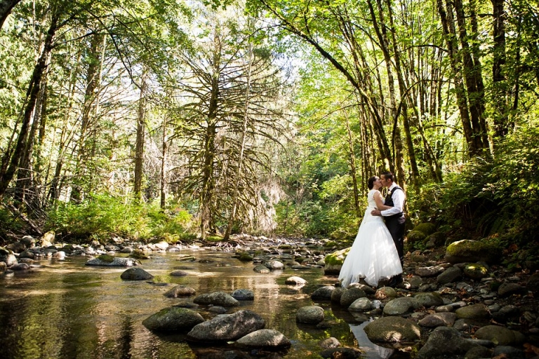 bride and groom standing on rock  by a stream