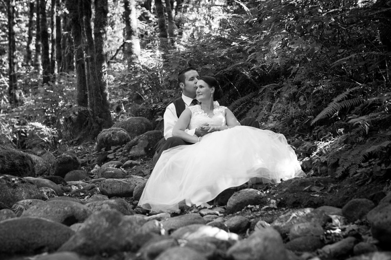 black and white photo bride and groom sitting by a stream