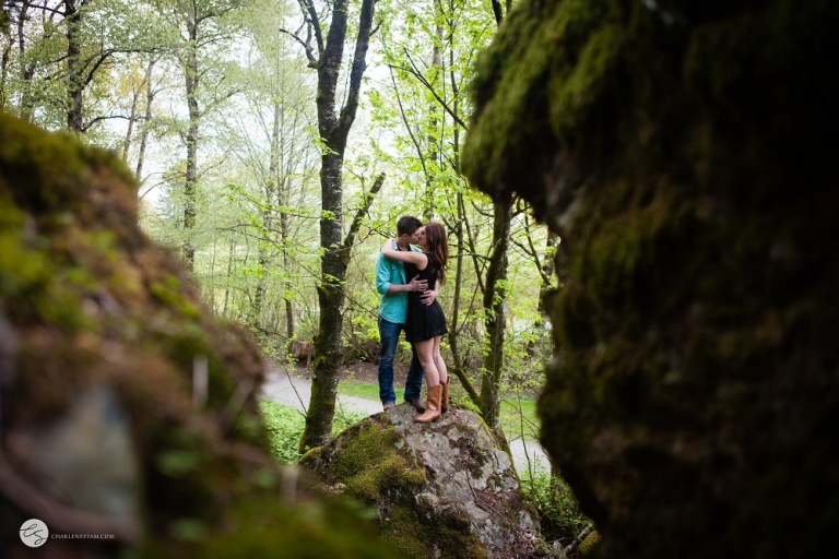 engaged couple kissing on a rock in the trees