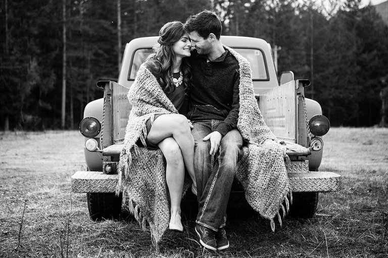 an engaged couple sitting in the box of a truck in a field