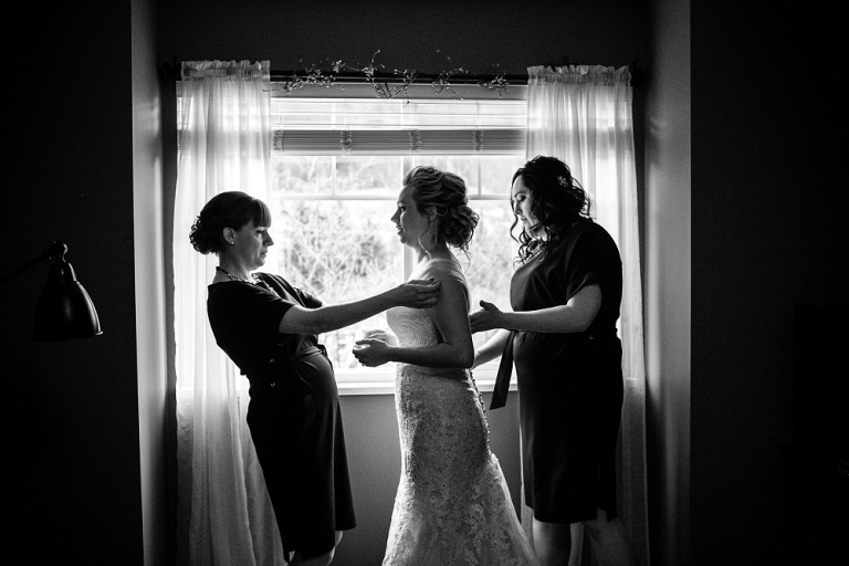 black and white photo of bridesmaids helping a bride get ready on the morning of her wedding