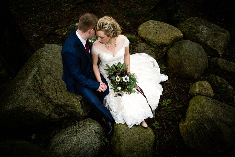 bride and groom sitting on rocks and snuggling