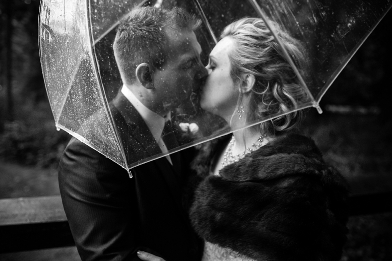 black and white photo of bride and groom kissing under umbrella