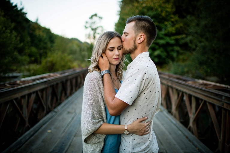 an engaged couple kissing on a bridge