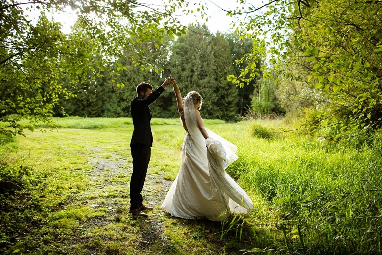 bride and groom dancing in grassy field with trees surrounding them
