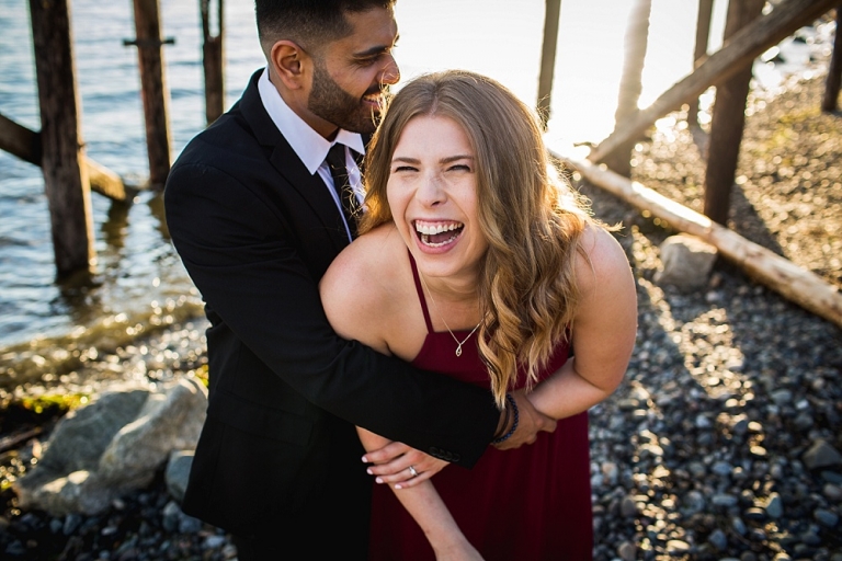 Girl in red dress laughing while boy in suit hugs her on the beach